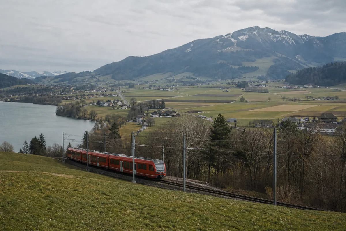 Un train régional traverse un paysage de lac et de collines.